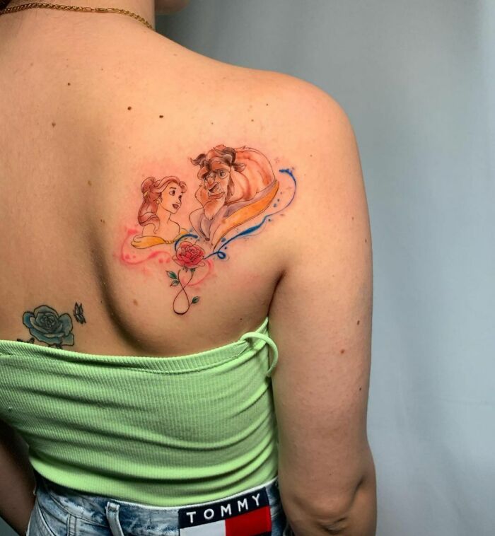 Watercolor tattoo on back, featuring ethereal Beauty and the Beast design in soft pastel hues.