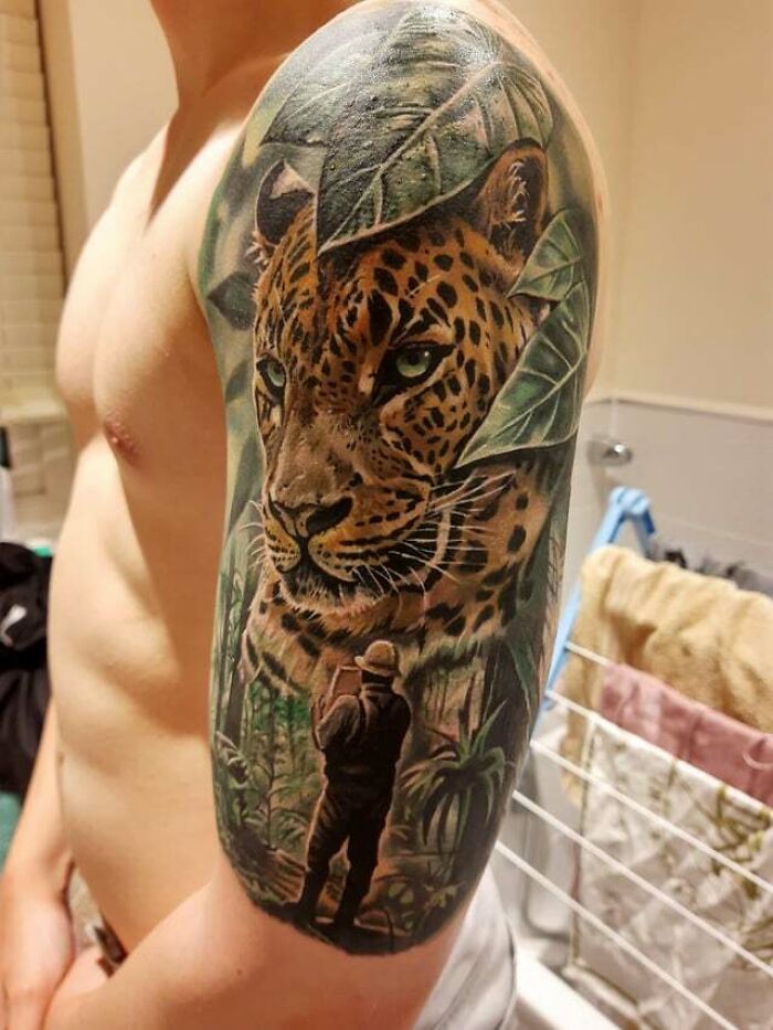 Detailed leopard tattoo on upper arm, featuring jungle and explorer elements; inspiring animal tattoo art ideas.