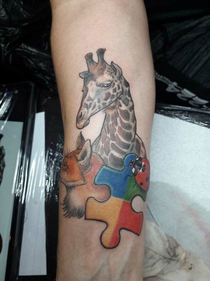 Animal tattoo featuring a giraffe, fox, ladybug, and colorful puzzle piece on an arm.