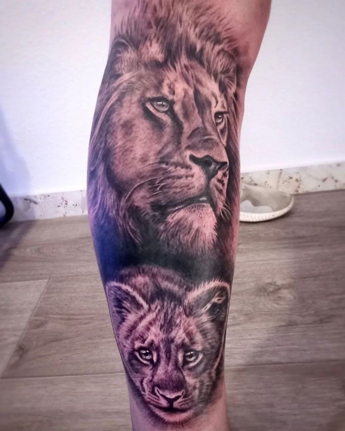 Lion tattoo on a leg, featuring detailed artwork of an adult lion and a cub, showcasing stunning animal tattoo design.