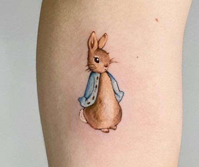 Cute rabbit tattoo design on forearm, featuring a brown bunny in a blue jacket. Perfect animal tattoo idea.