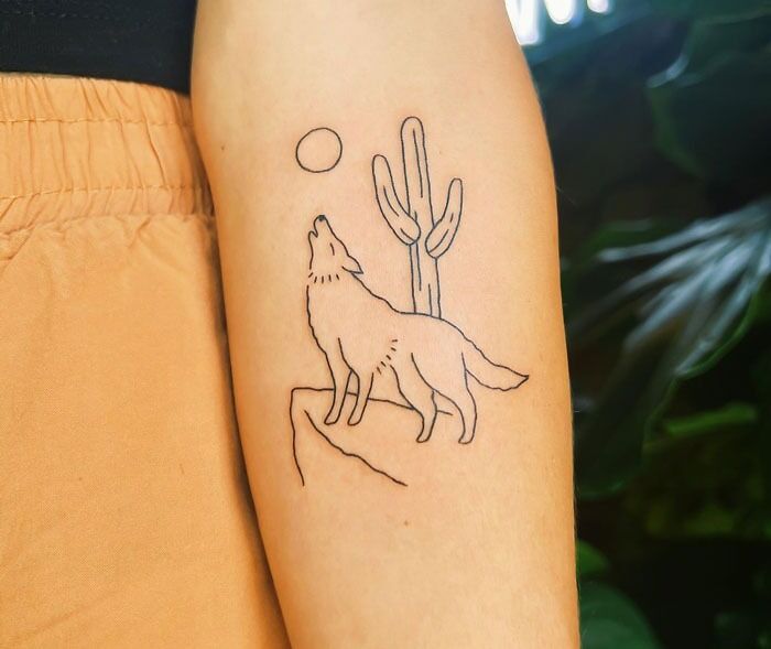 Minimalist wolf tattoo on arm, featuring a cactus and moon, showcasing animal tattoo ideas.
