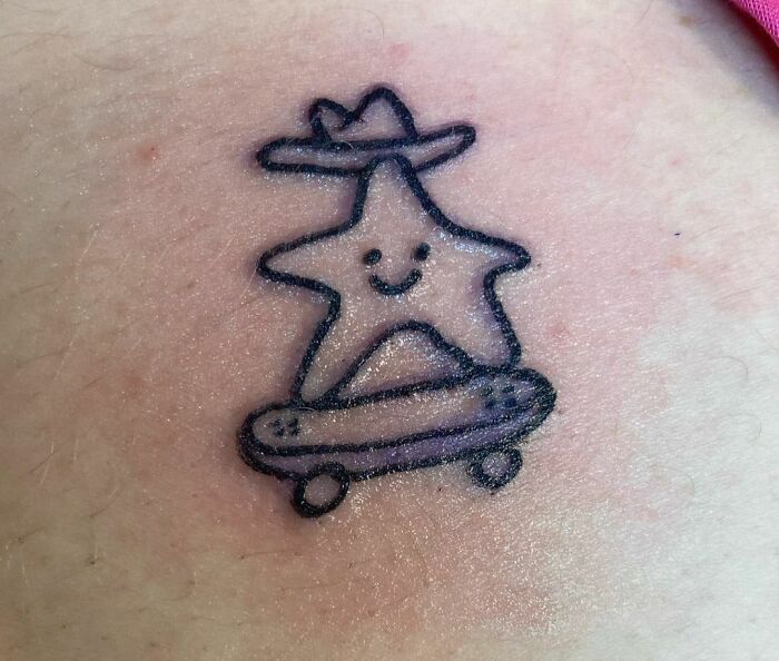 Funny tattoo of a smiling star on a skateboard wearing a hat.