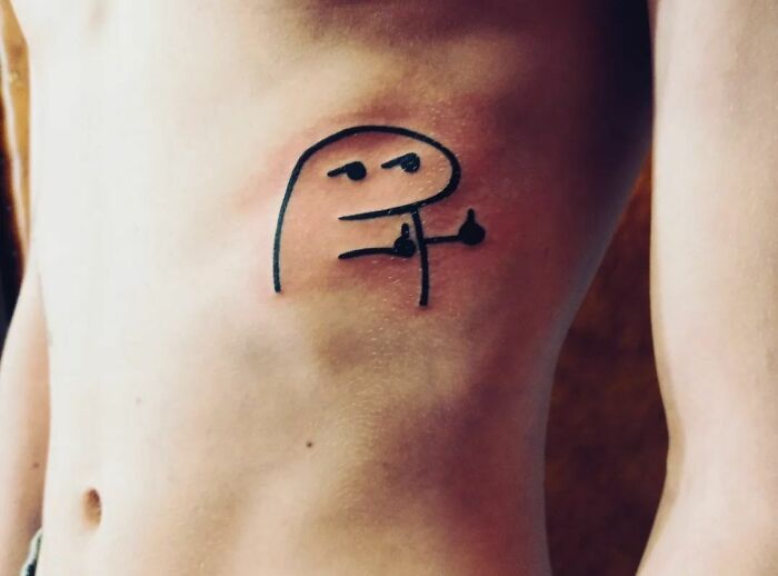 Funny tattoo of a simple cartoon character giving two thumbs up on a person's ribcage.