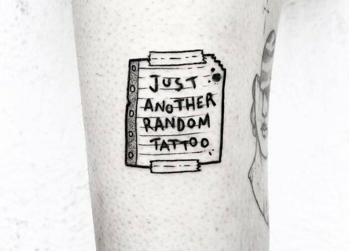 Funny tattoo on skin with text "Just Another Random Tattoo" on lined paper design.