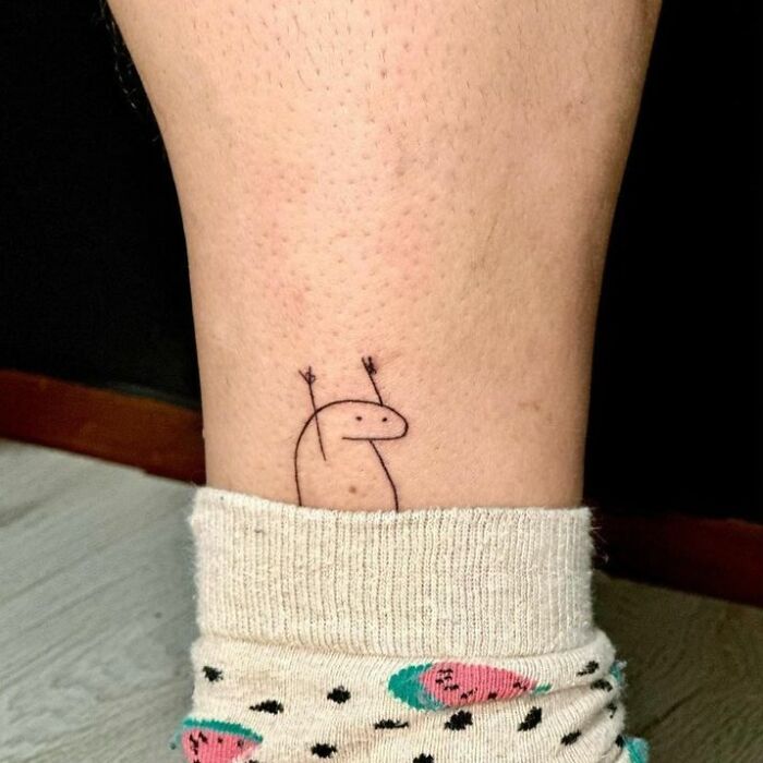 Simple funny tattoo of a stick figure dinosaur on a leg above a watermelon-patterned sock.