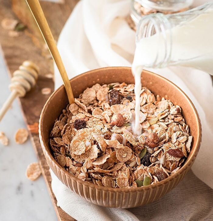 Pouring milk in cereal bowl with raisins and nuts 