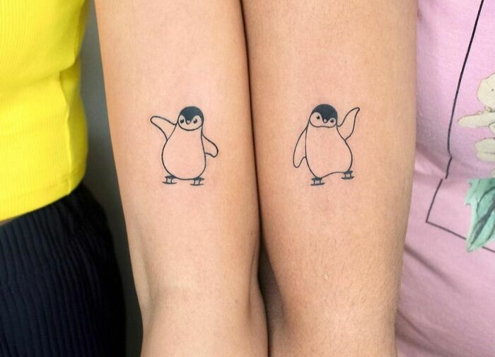 Matching penguin BFF tattoos on two arms, symbolizing friendship.
