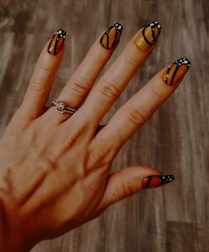 Hand with butterfly wing nail art design featuring orange, black, and white colors showcasing creative nail art ideas.