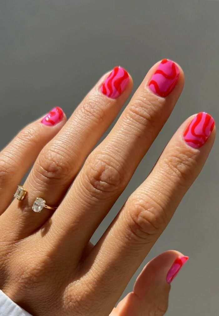 Hand with pink and red wavy nail art design, showcasing creative and trendy nail art ideas on natural nails.