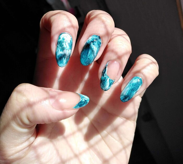 Hand with marble blue and white nail art ideas featuring long, curved nails in natural light showing texture details.