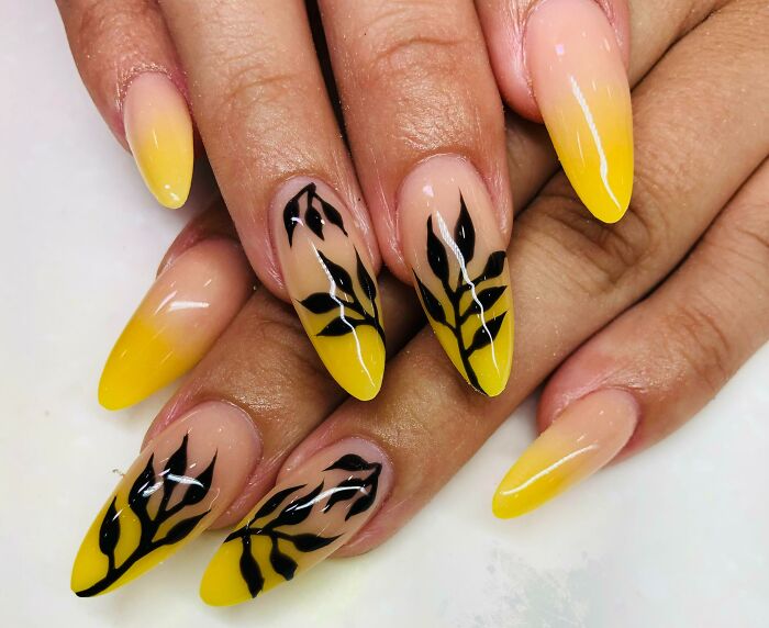 Yellow gradient nail art with black leaf designs on almond-shaped nails, showcasing creative nail art ideas and tiny artworks.