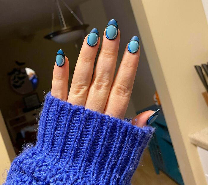 Hand with blue and black abstract nail art design, showcasing creative nail art ideas and unique tiny artworks on nails.