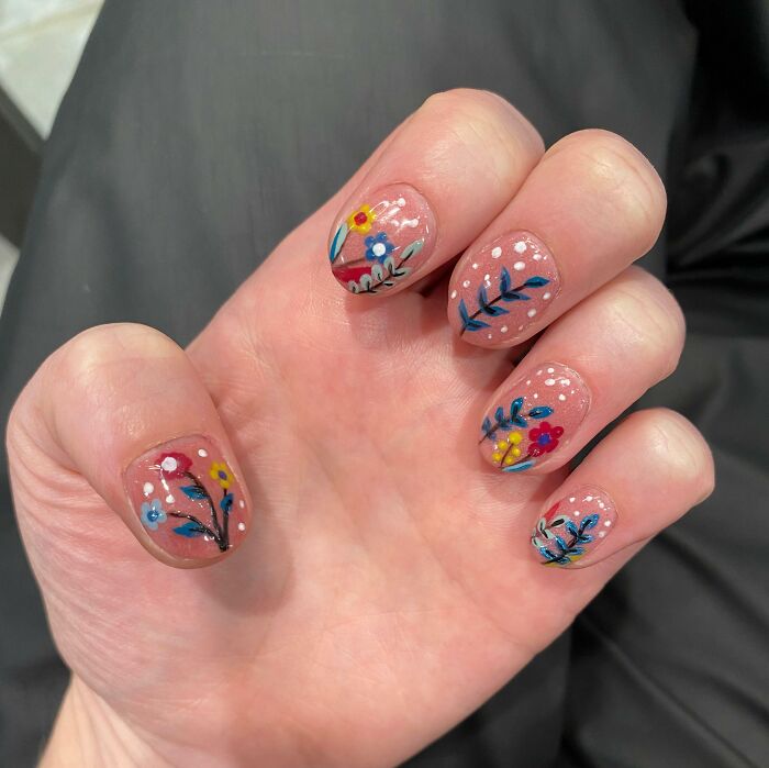 Hand with floral nail art designs on natural nails featuring small colorful flowers and white dots, showcasing creative nail art ideas.