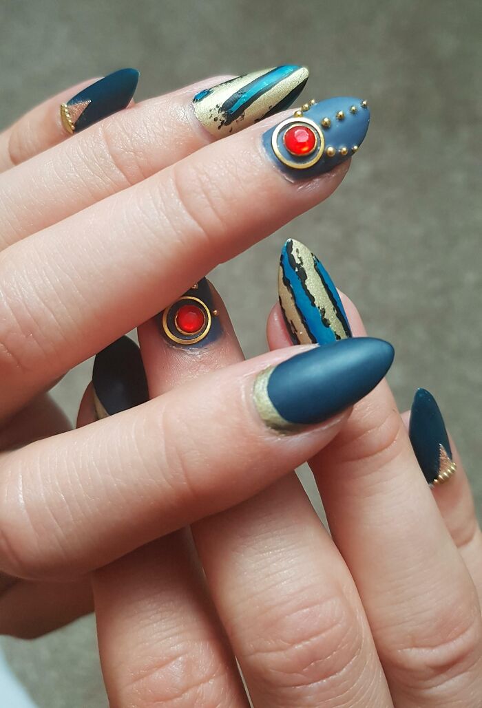 Matte blue and gold nail art with red gem accents and intricate striped designs, showcasing unique nail art ideas.