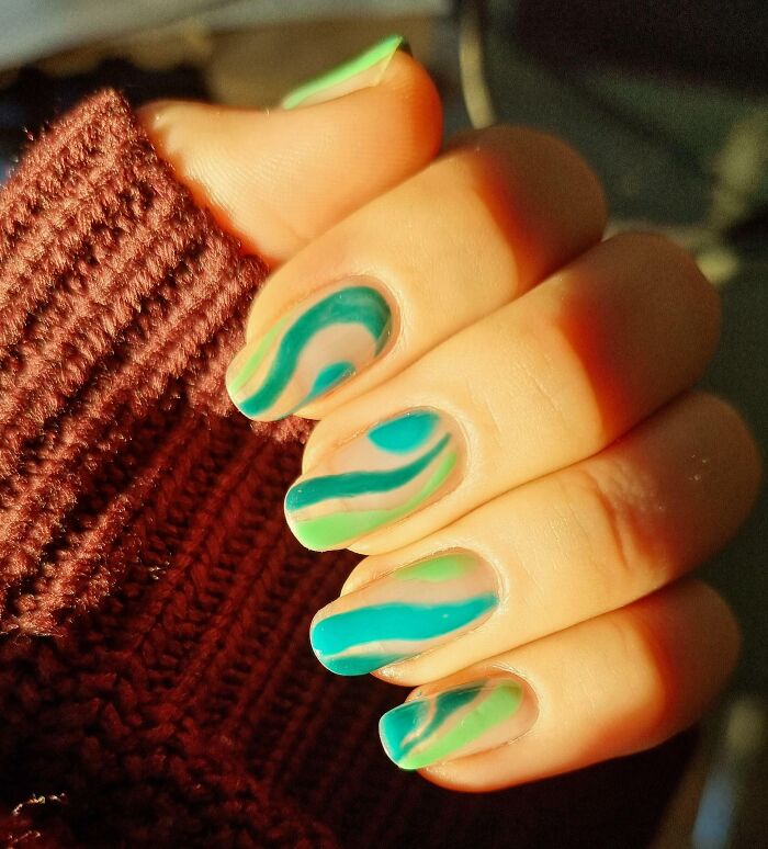 Close-up of hand with green and blue abstract nail art designs showcasing creative nail art ideas.