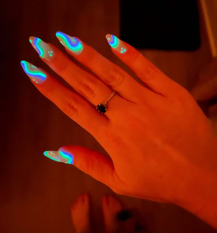 Hand with long nails featuring glowing blue and green abstract nail art ideas under dim lighting.