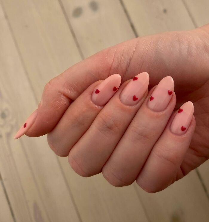 Close-up of nails with delicate nail art featuring small red hearts on a soft pink base, showcasing creative nail art ideas.