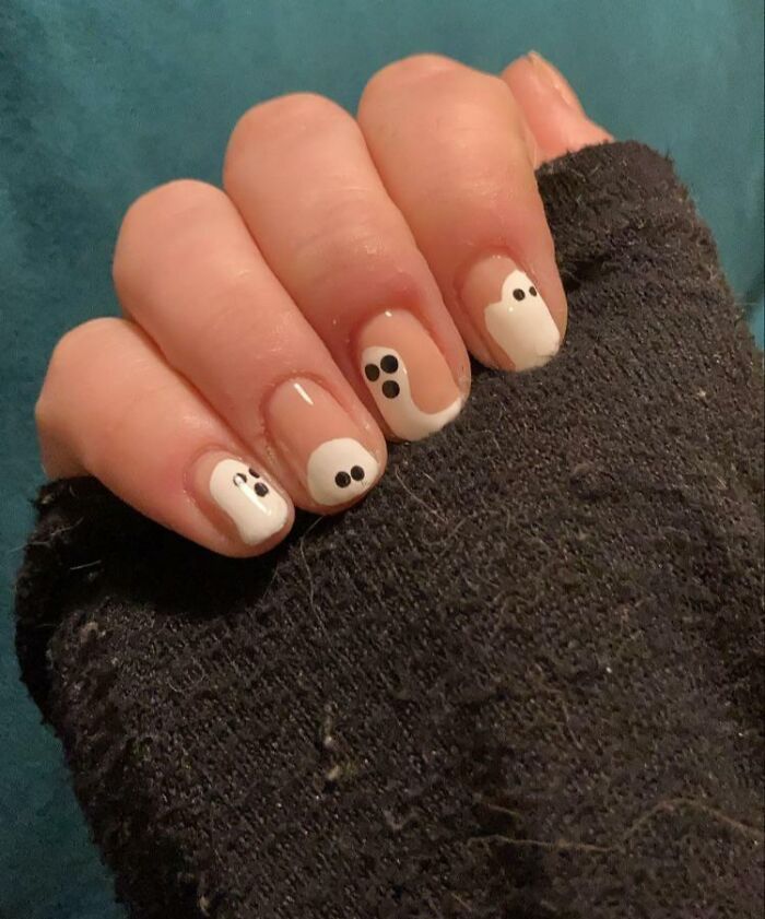 Nail art ideas featuring cute ghost designs on short nails with white and black polish against a dark textured fabric background.