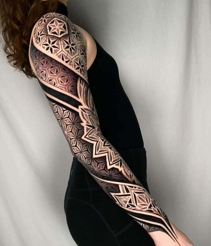 A person with an intricate geometric tattoo sleeve featuring various shapes and forms.