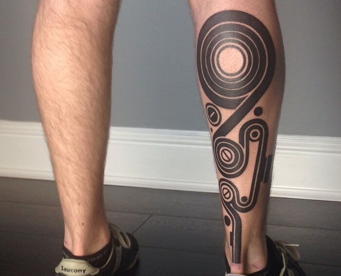 Geometric tattoo with black circular patterns on calf, showcasing creativity.