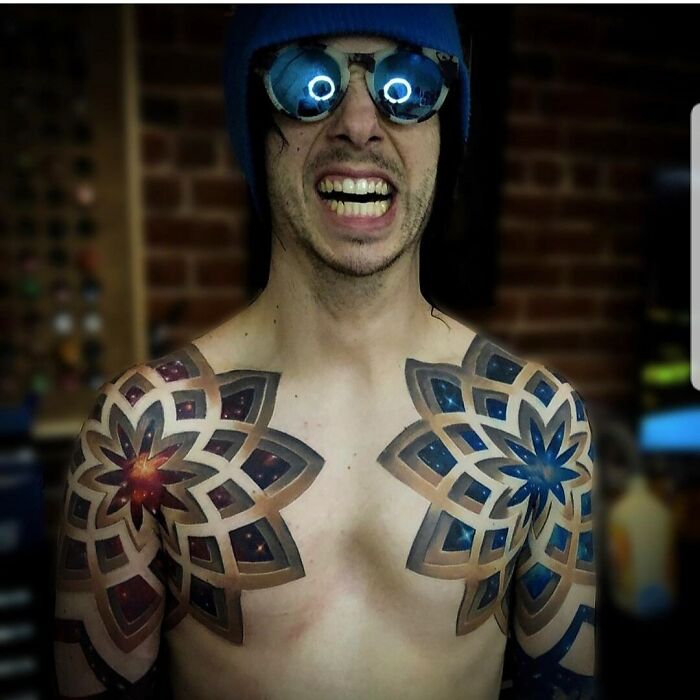 Man with geometric tattoos on shoulders, wearing sunglasses and a blue hat, expressing creativity.