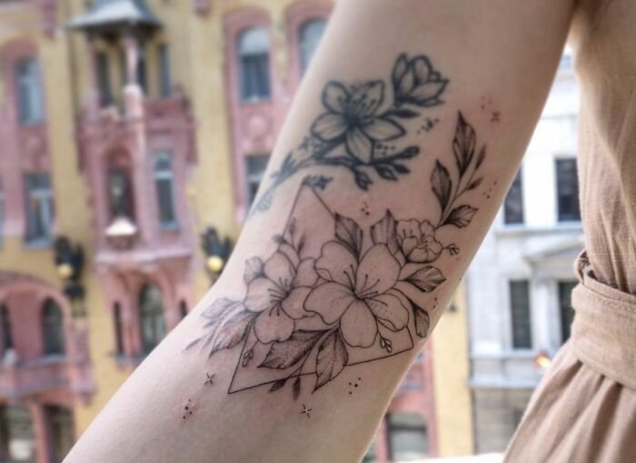 Floral geometric tattoo on a forearm with city buildings in the background.