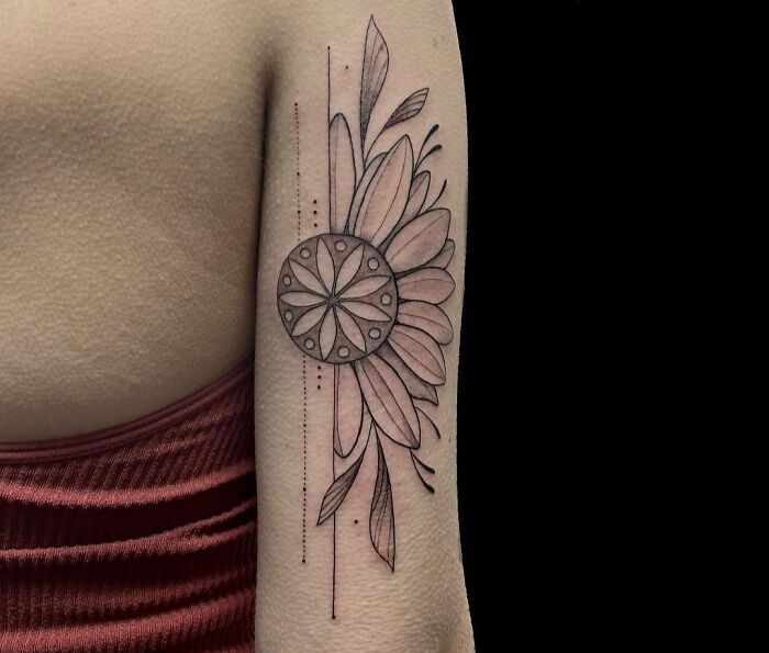 Geometric tattoo on an arm featuring a circular floral design with linear accents in black ink.