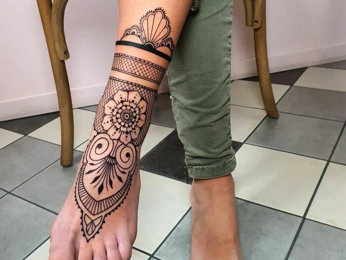Geometric tattoo on the foot and lower leg featuring intricate circular and floral patterns.