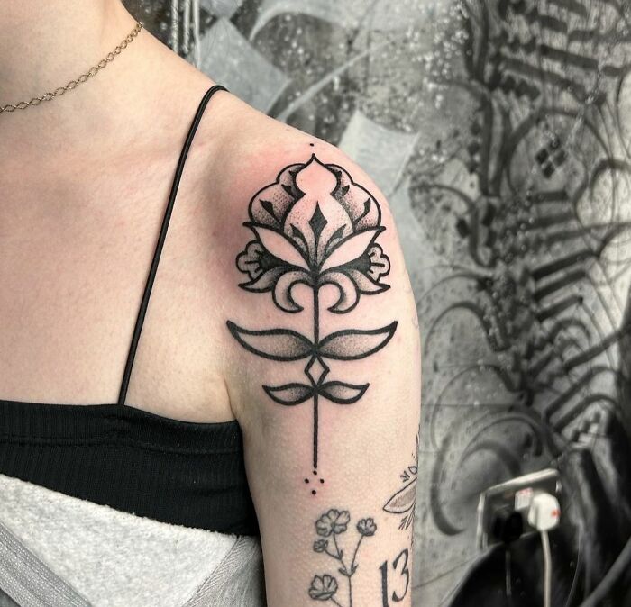 Geometric tattoo of a stylized flower on the shoulder, featuring intricate black line designs.