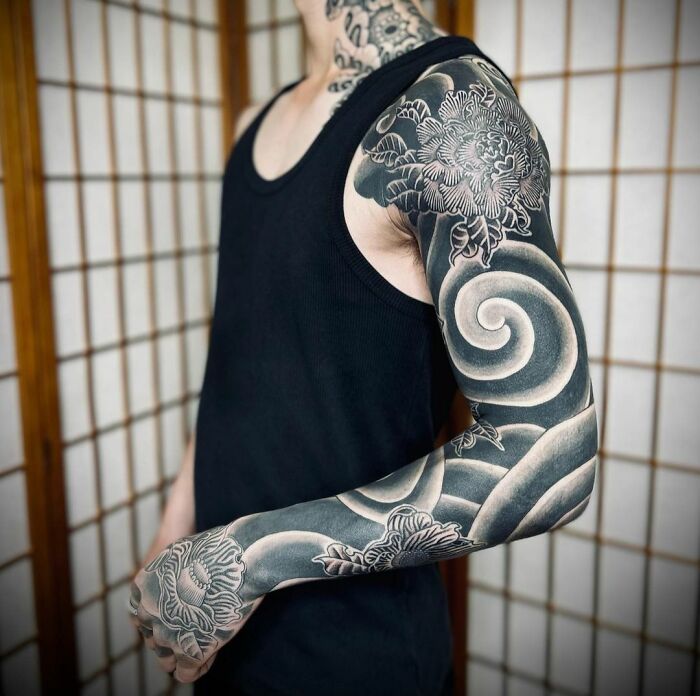 Person with a geometric tattoo sleeve featuring intricate shapes and forms, wearing a black tank top.