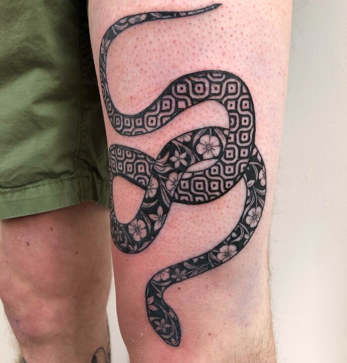 Geometric tattoo of a snake with floral patterns on a person's leg.