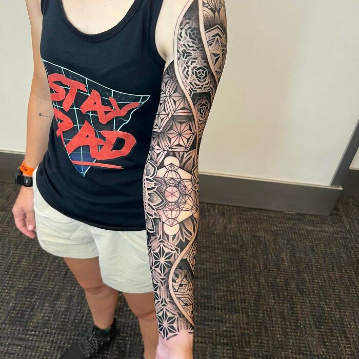 Person with a detailed geometric tattoo sleeve showing intricate patterns on their arm, wearing a "Stay Rad" tank top.