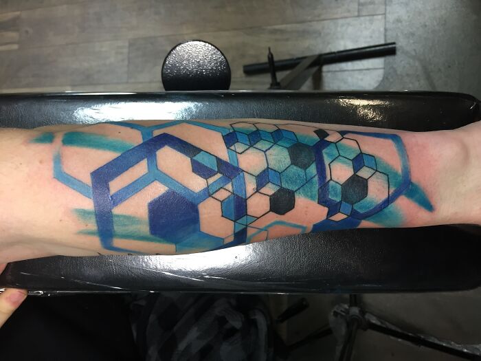 Blue and black geometric tattoo design on forearm featuring hexagonal and cube patterns.