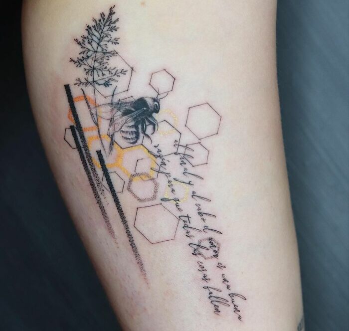 Geometric tattoo with a bee, hexagons, and cursive script on skin.