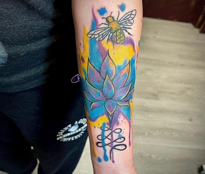 Colorful geometric tattoo with bee and lotus design on forearm.