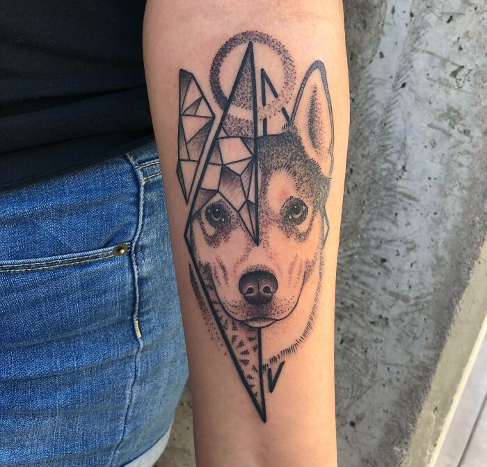 Geometric tattoo of a dog's face with angular patterns on an arm.