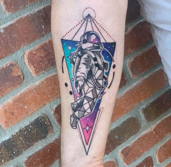 Geometric tattoo of an astronaut with colorful patterns, inked on a forearm.