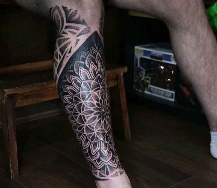 Geometric tattoo design on leg, featuring intricate shapes and forms in a black ink pattern.