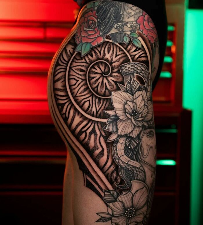 Geometric tattoo on thigh featuring intricate patterns and floral elements against a colorful background.