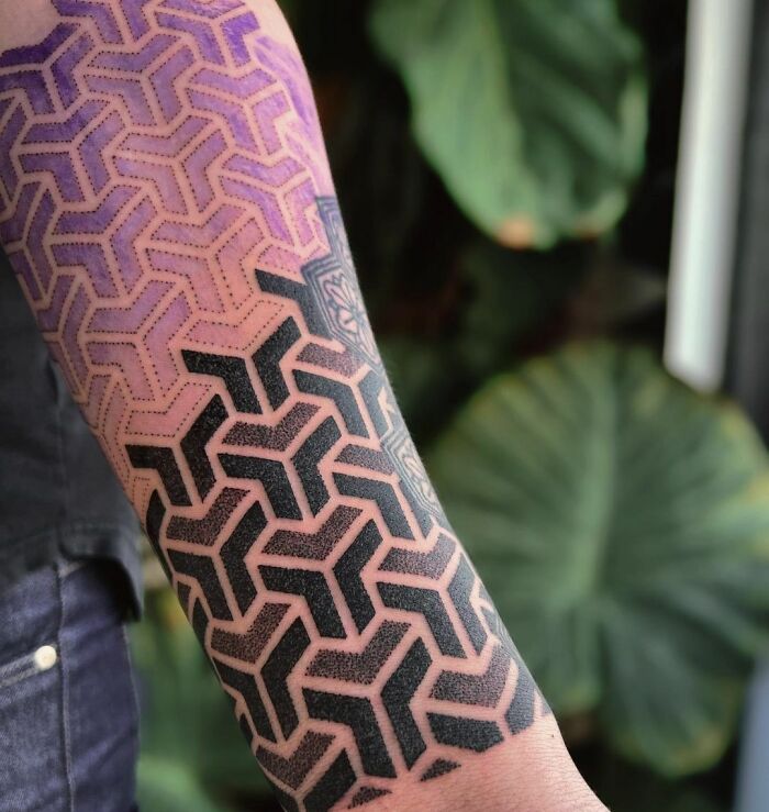 Arm with geometric tattoo, featuring intricate patterns and shapes in black and purple.