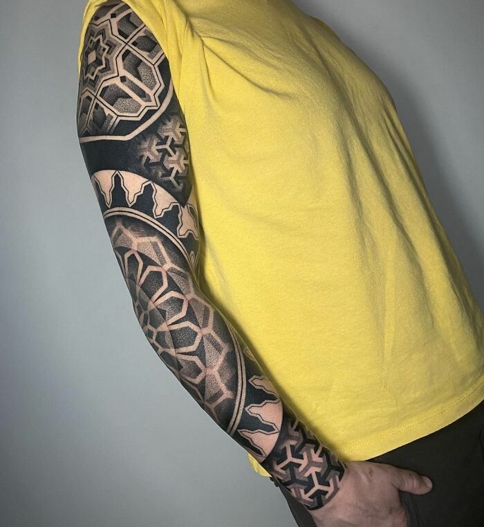 Geometric tattoo sleeve featuring intricate shapes and forms on a person's arm wearing a yellow shirt.
