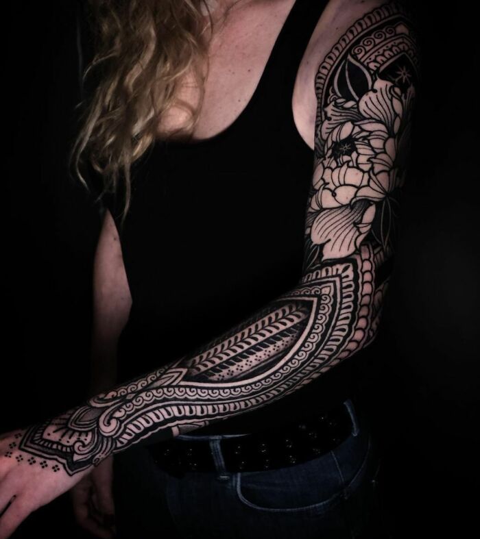 Sleeve with intricate geometric tattoo design on arm, featuring patterns and floral elements.