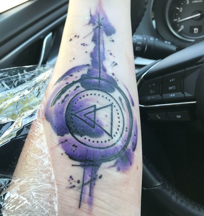 Vibrant geometric tattoo with purple and black ink featuring abstract shapes on forearm.