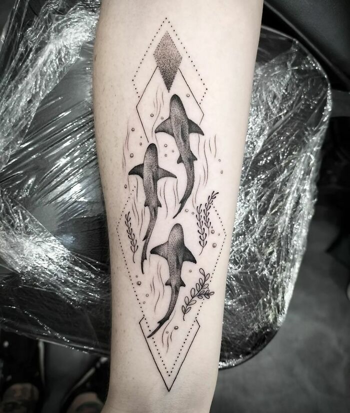 Geometric tattoo featuring three stylized sharks within diamond shapes on forearm.