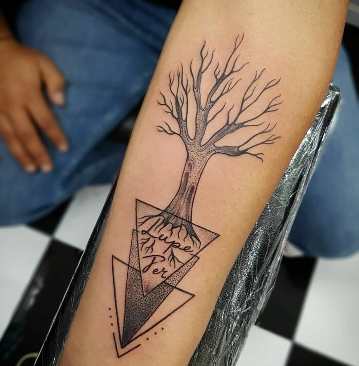 Arm with geometric tattoo featuring a stylized tree and triangles, highlighting creativity.