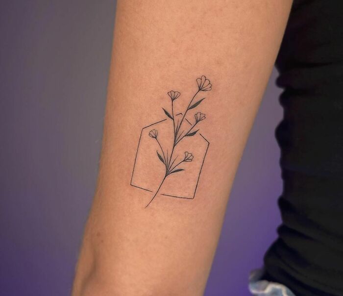 Geometric tattoo with flowers inside a hexagon outline on a person's forearm.