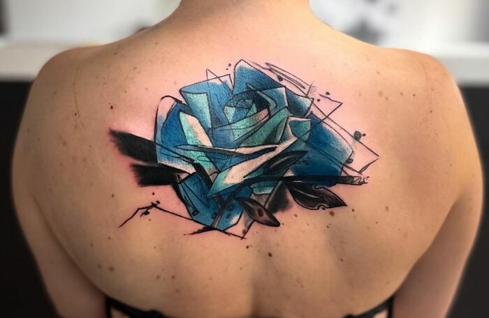 Geometric tattoo design featuring abstract blue shapes on a person's upper back.