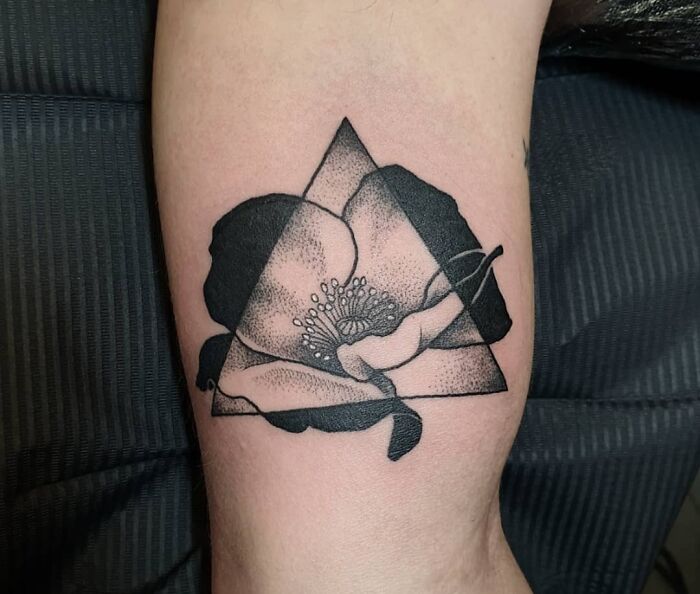 Geometric tattoo of a floral design within a triangle on skin.
