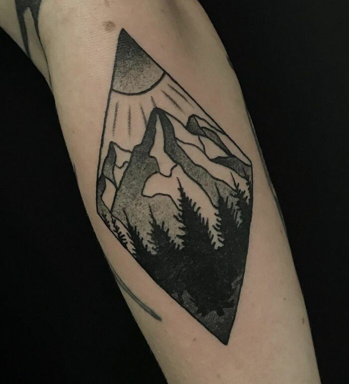 Geometric tattoo of mountains and trees in a diamond shape on arm.